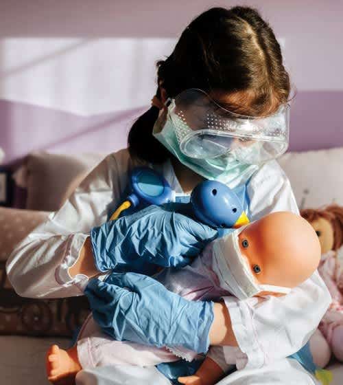 Little girl playing with doll wearing mask