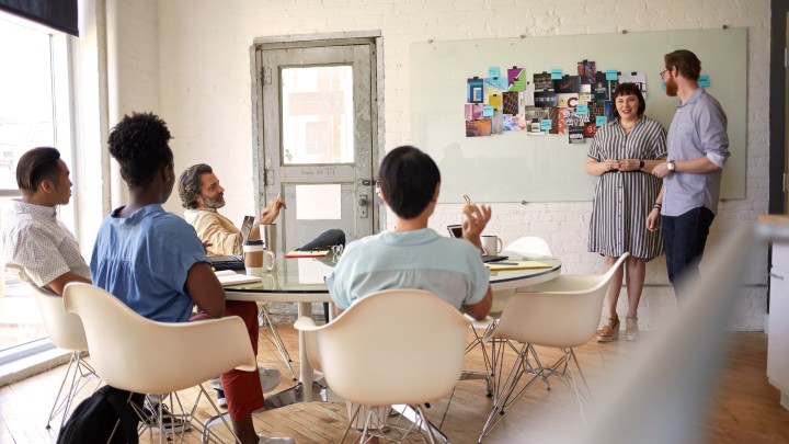 Employees sitting around a table while two people present.